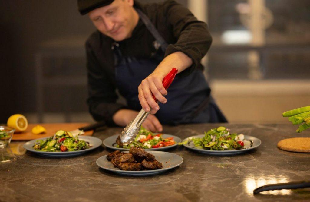 Un chef cuisinier dresse des assiettes raffinées garnies de salades fraîches pour concevoir une idée menu de mariage végétarien gastronomique.