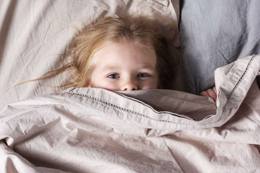 Un enfant effrayé émergeant de sous sa couette, les yeux grands ouverts, en pleine terreur nocturne.